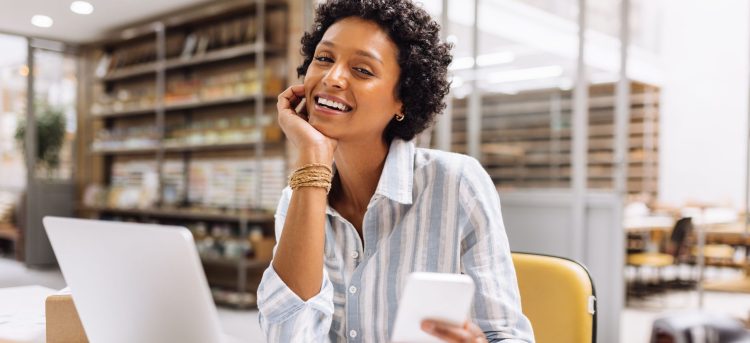 Successful online store owner smiling at the camera while working in a warehouse. Happy female entrepreneur managing online orders on her website. Businesswoman running an e-commerce small business.